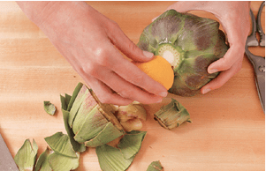 Hands rubbing lemon on cut artichokes to prevent browning. 