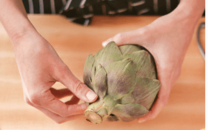 Hands removing artichoke leaves. 