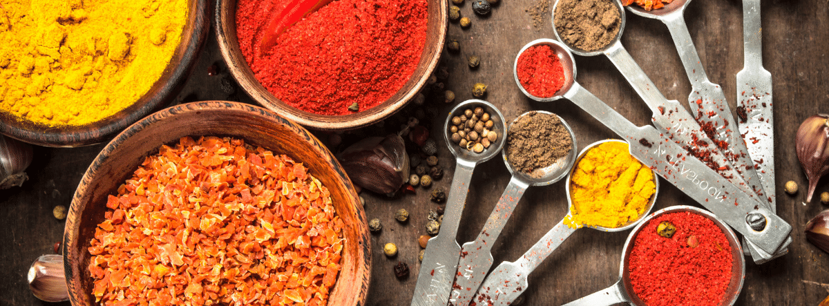 variety of coloured spices in jars and measuring spoons