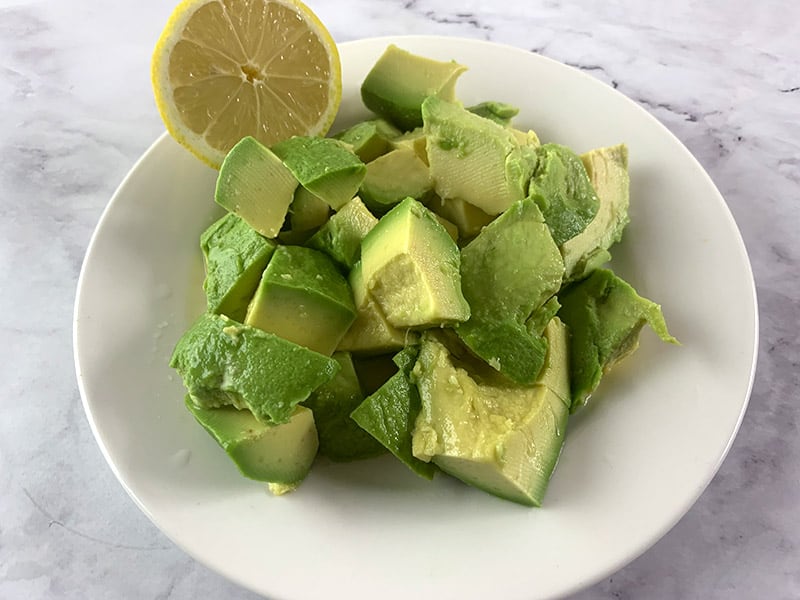 Diced Avocado on a white plate with lemon. 