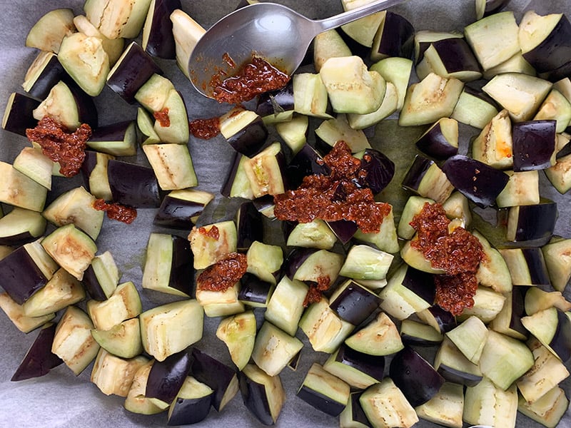 Cubed eggplant on a baking tray with harissa and oil. 
