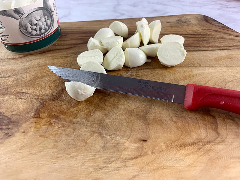 Mini bocconcini balls being sliced in half on a wooden board with a red knife. 