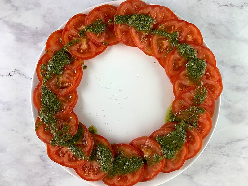 Sliced tomatoes on a white plate with pesto drizzled on top. 