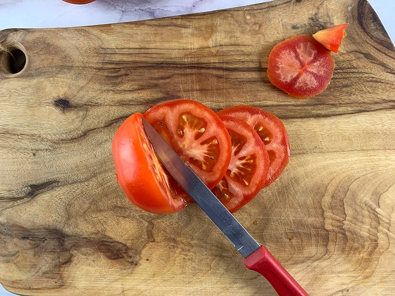 A red knife slicing tomatoes on a wooden board. 