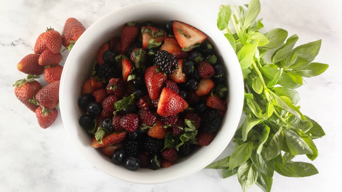 SUMMER BERRIES IN A WHITE BOWL WITH STRAWBERRIES AND BASIL ON THE SIDE