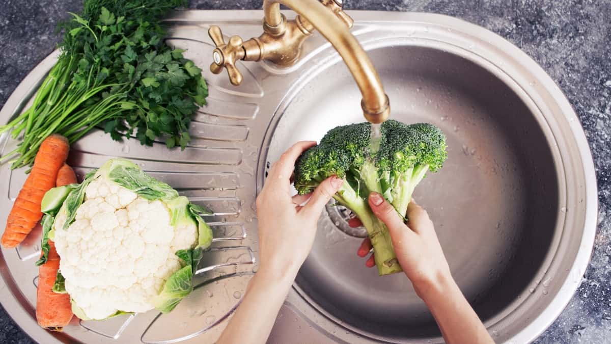 Hands rinsing broccoli in the sink.
