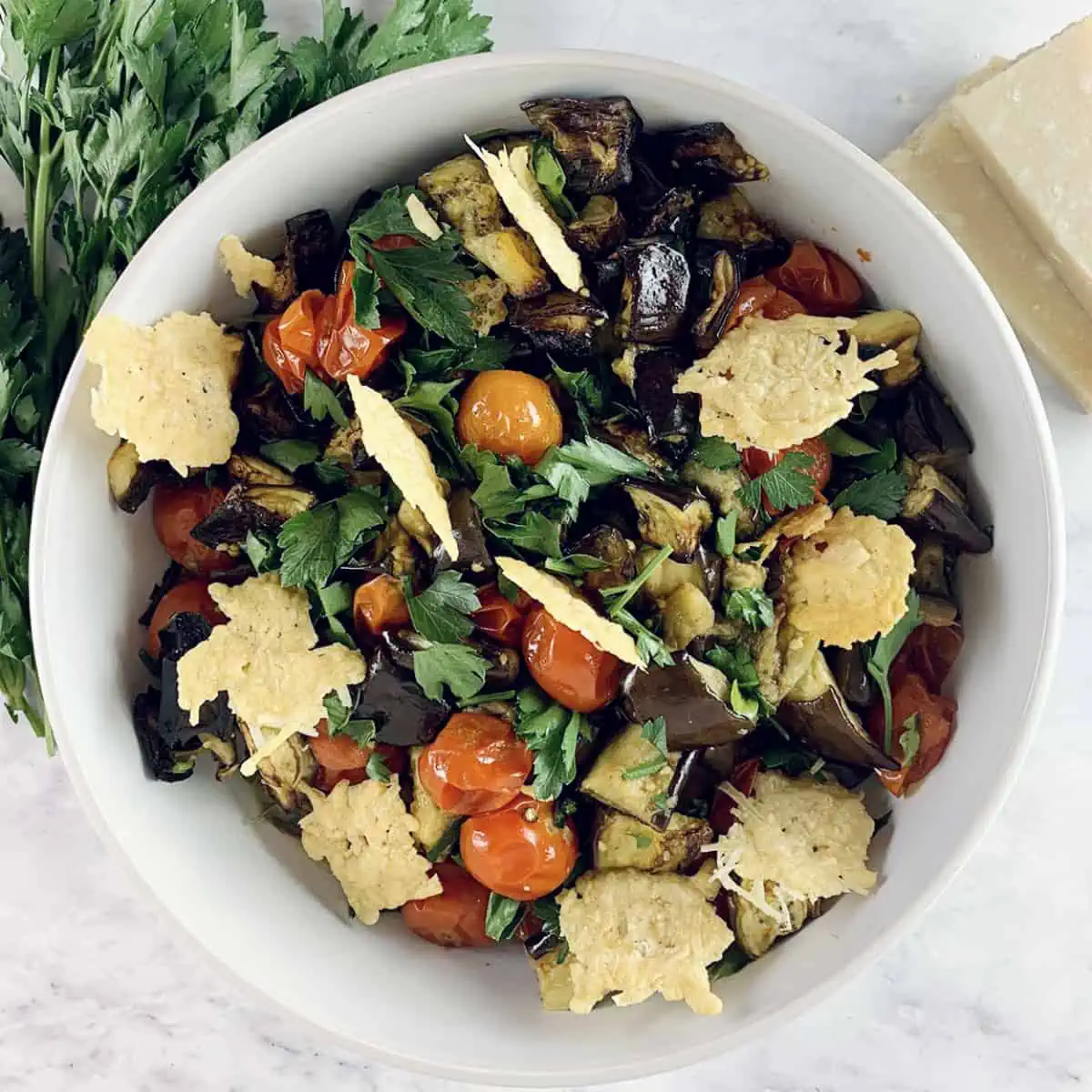 Mediterranean roasted eggplant salad in a white bowl with parsley and parmesan on the side.