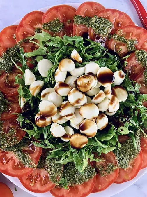 A close-up of a tomato mozzarella salad with rocket or arugula drizzled with some balsamic. 