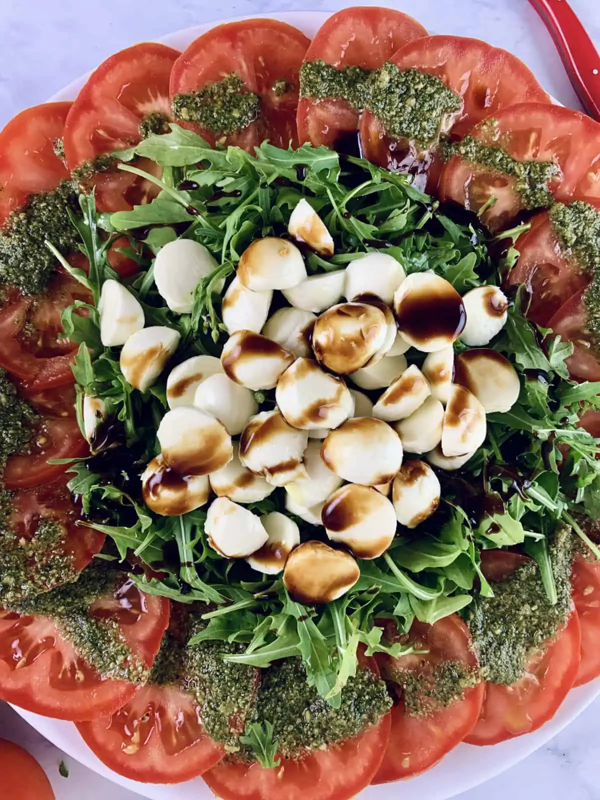 A close of tomato mozzarella salad with rocket or arugula drizzled with balsamic.
