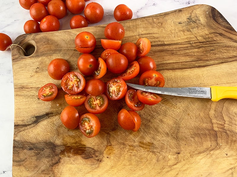 CHOPPED CHERRY TOMATOES ON WOODEN BOARDY WITH KNIFE