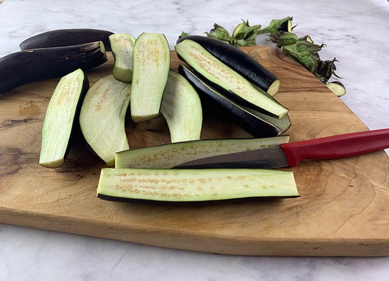 A knife sitting on top of a wooden cutting board with sliced Eggplant.