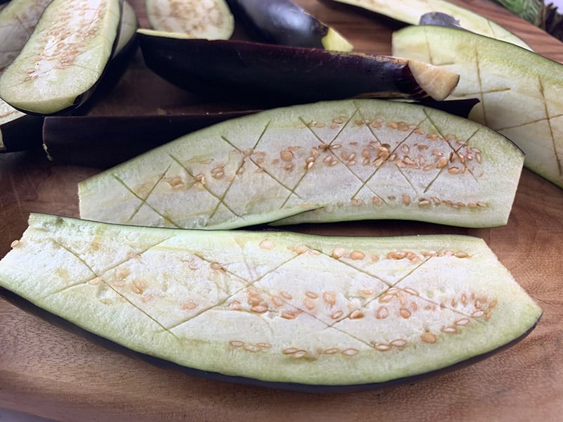 Long eggplant halves with the flesh being scored in a cross-hatch pattern. 