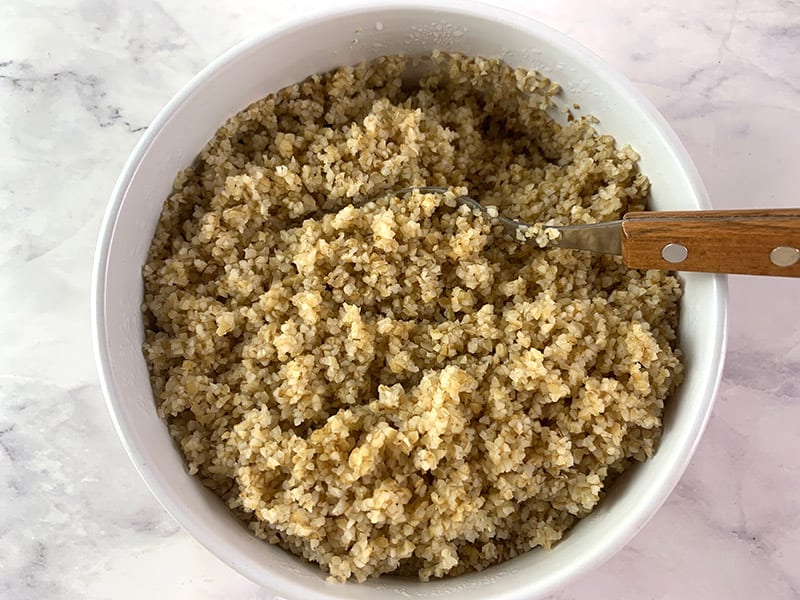 Fluffing up cooked bulgur wheat with a fork in a white bowl.