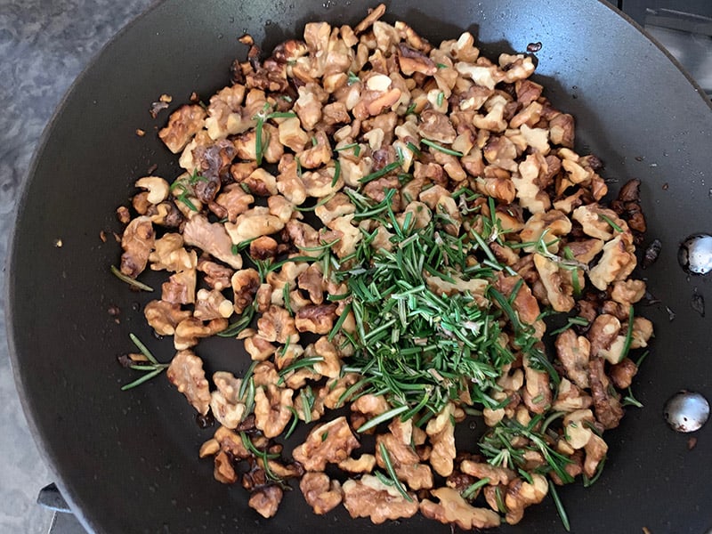 Golden brown walnuts in a frypan with fresh chopped rosemary. 