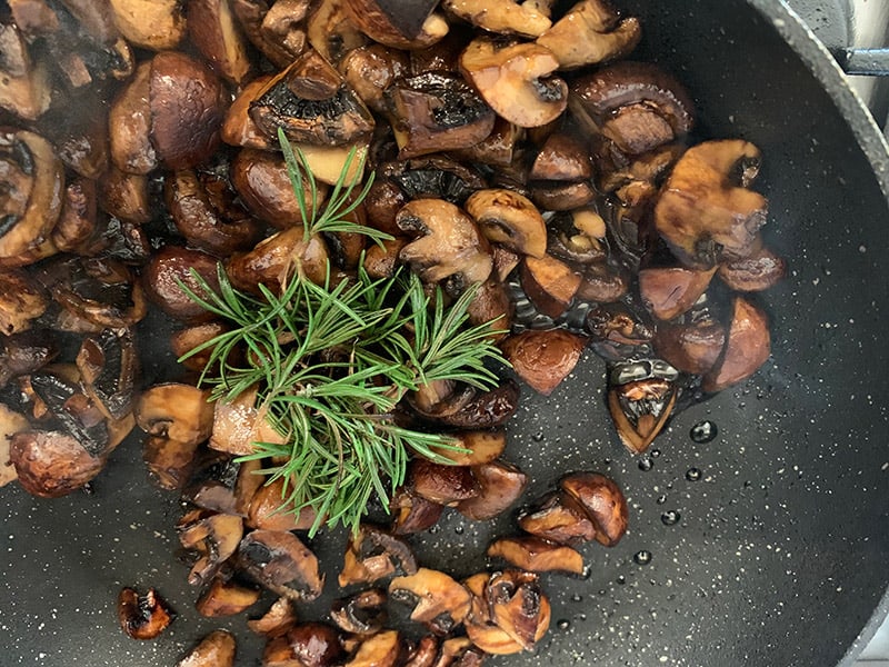 Sauteed mushrooms in a pan with rosemary sprigs. 