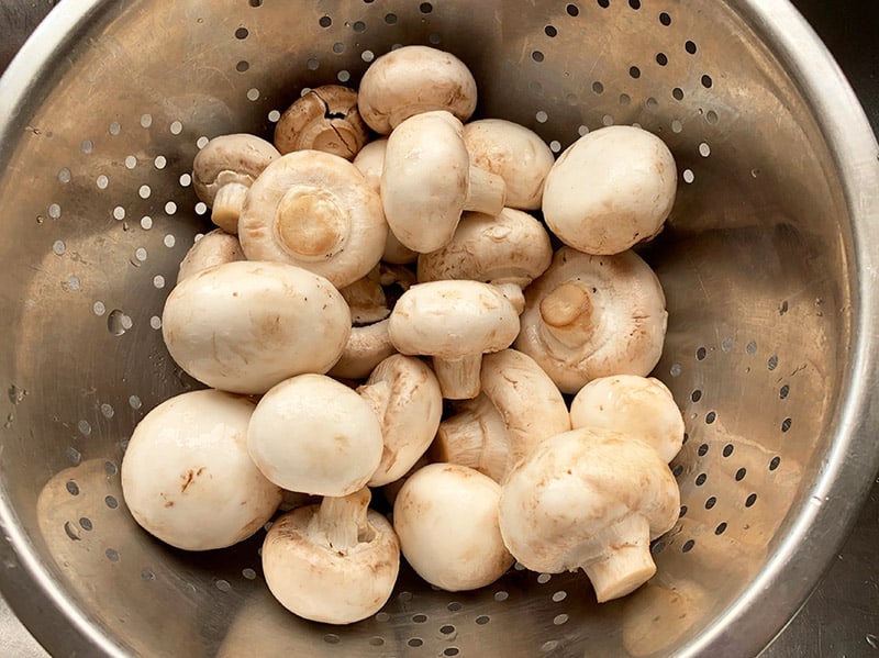 Straining white mushrooms in a colander in the sink. 