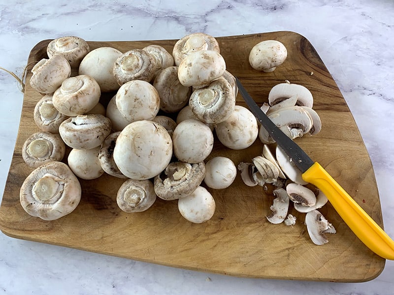 Slicing washed white mushrooms on a wooden board with a knife. 
