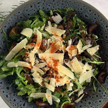 A bowl of salad with balsamic Mushroom salad and shaved parmesan.