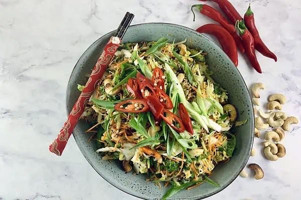 Chinese cabbage salad in a grey ceramic bowl with red chopsticks on the side. Red chillies and on right side.