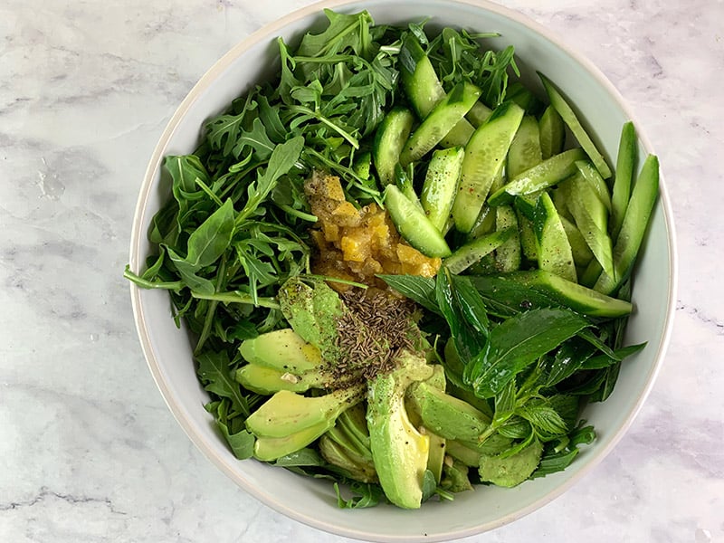 Prepared arugula, and avocado salad ingredients in a white bowl. 