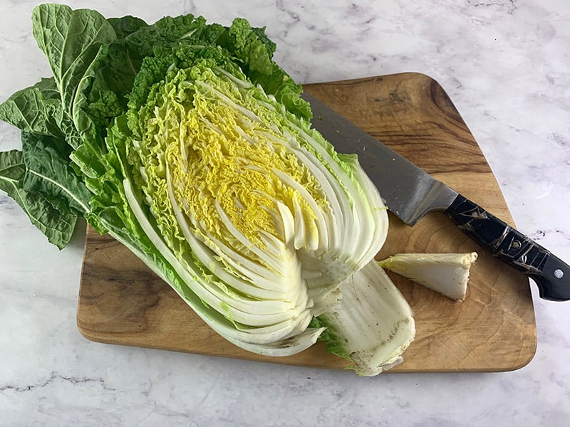 A napa or Chinese cabbage half with its core removed on a wooden board with a knife. 