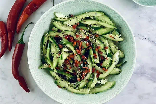 A close-up Chinese cucumber salad in a mint bowl with chillis on the side.