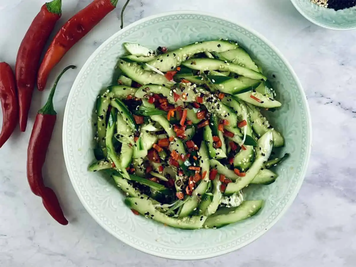 A close-up Chinese cucumber salad in a mint bowl with chillis on the side.