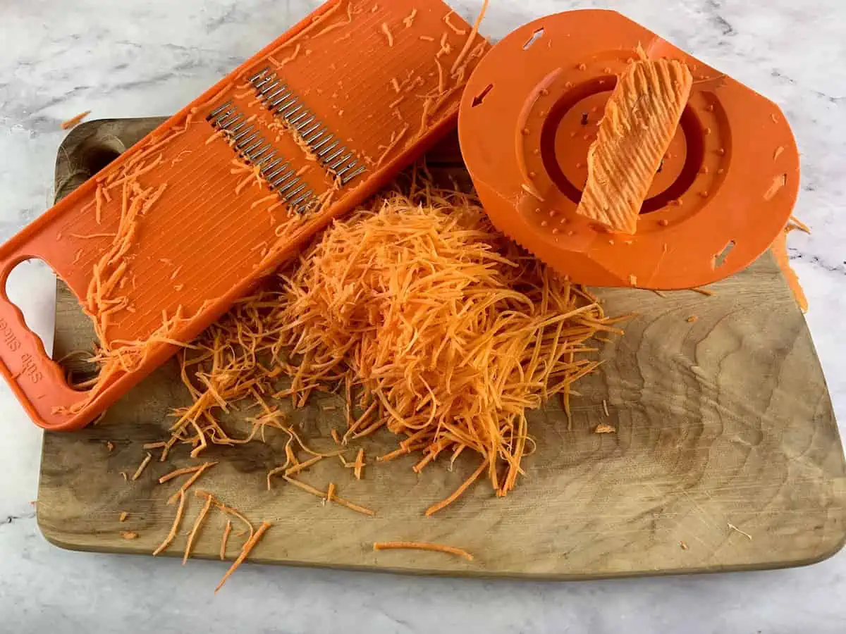 Carrots are being cut into fine julienne with an orange mandoline slicer.