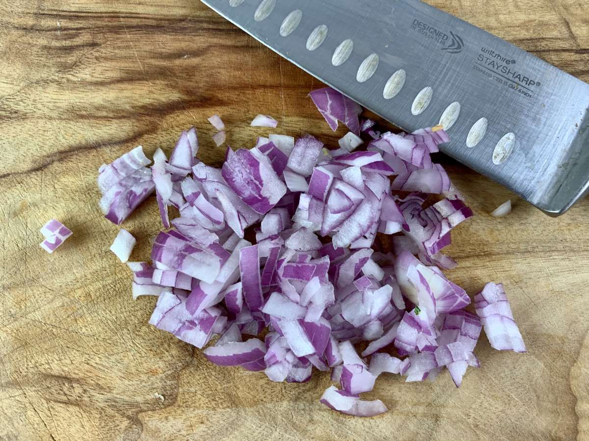 Dicing red onion on a wooden board with a knife.