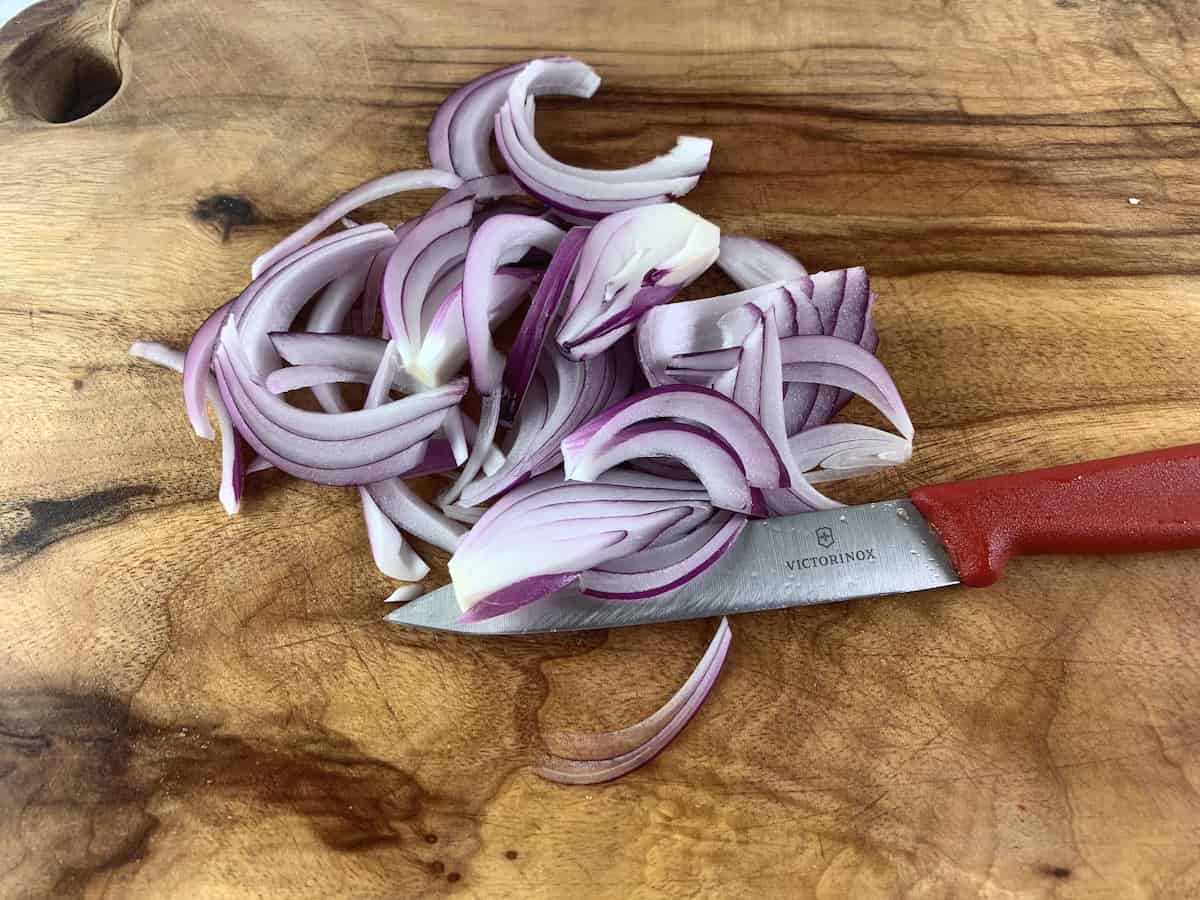 Cutting red onion into slices on a wooden board with a knife. 