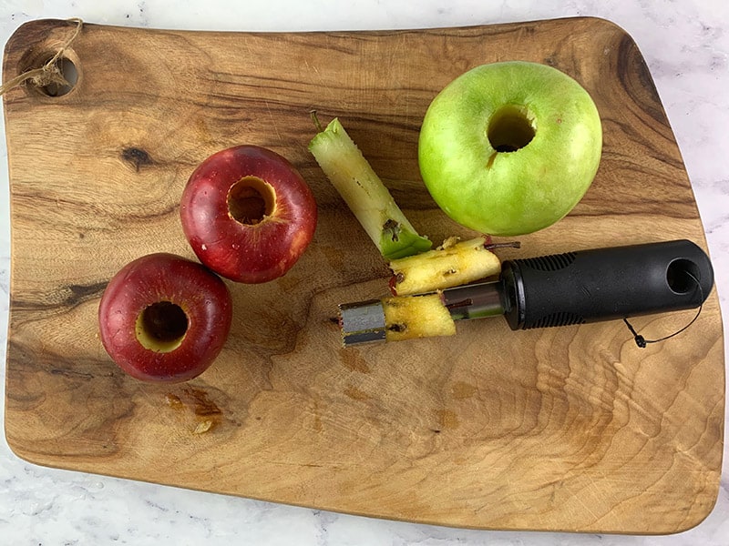 CORING RED AND GREEN APPLES WITH AN APPLE CORER ON A WOODEN BOARD