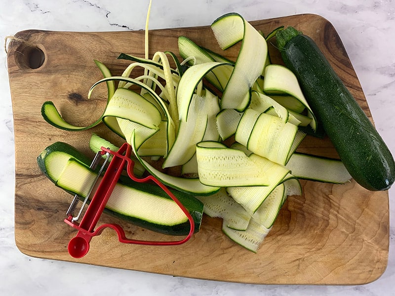 USING A VEGETABLE PEELER TO CUT ZUCCHINI INTO RIBBOSN