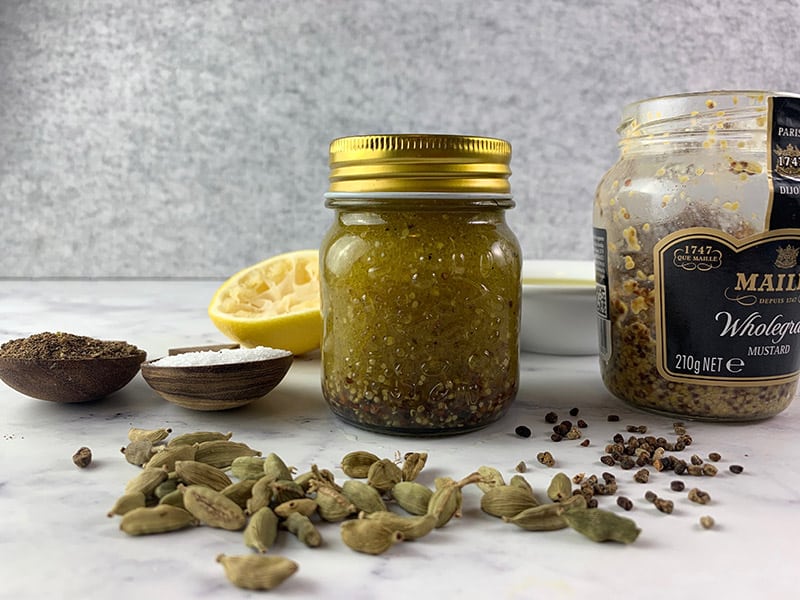 Shaken Cardamom vinaigrette in a glass jar with ingredients scattered about. 