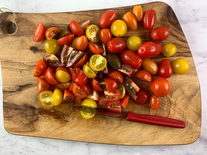 An aerial view of a cherry tomato medley being sliced in half on a wooden board.