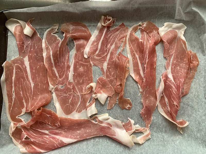 Raw prosciutto slices on a lined baking tray.