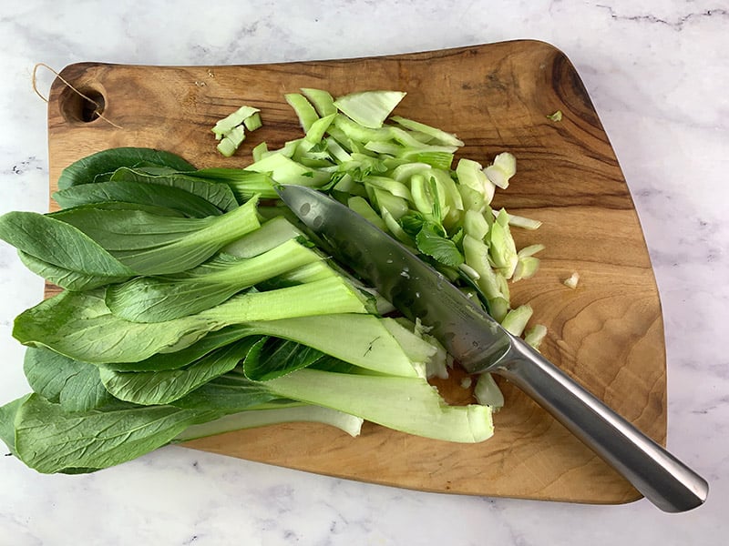 Diagonally cutting pak choy on a wooden board with a knife. 