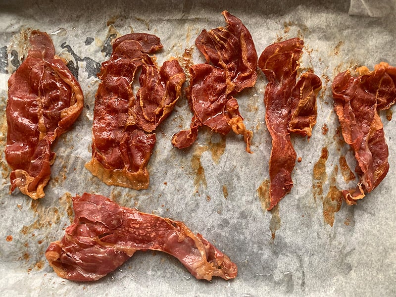 Prosciutto slices on a lined baking tray that have been roasted until crisp.