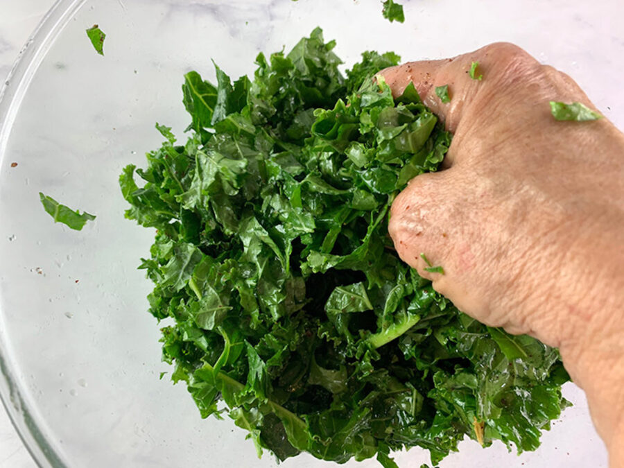 Hands massaging kale in a bowl with dressing. 