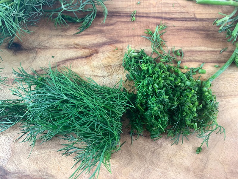 Chopping dill on a wooden board.