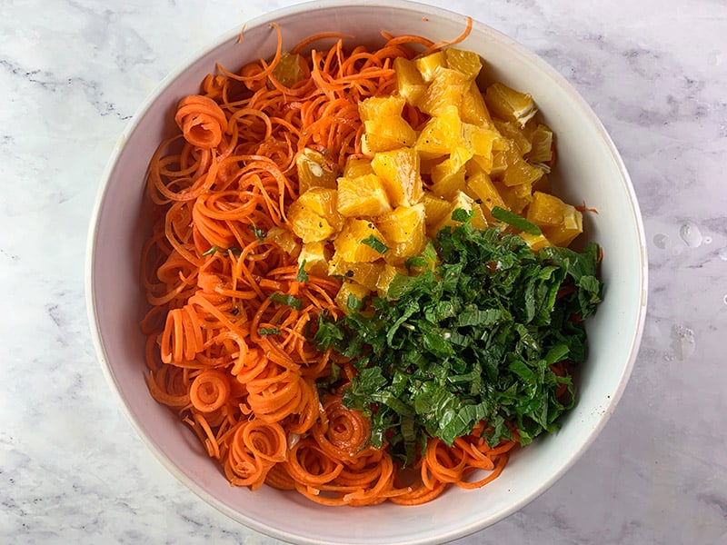 Prepared carrot and orange salad ingredients in a white bowl. 