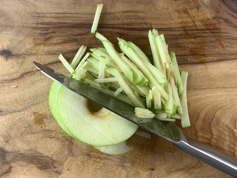 A knife cutting apple slices into thin julienne. 