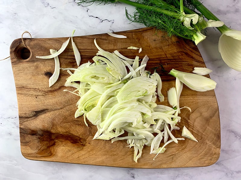 Thinly sliced fennel sitting on a wooden board. 