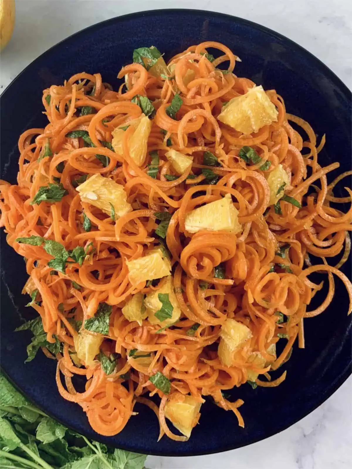 A close up of spiral carrot & orange salad on a navy blue plate.