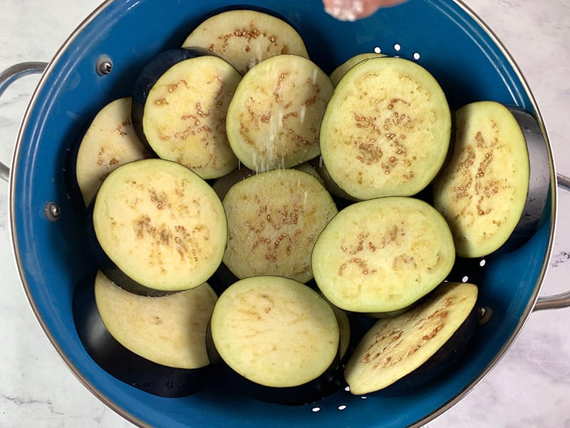 LAYERS OF EGGPLANT ROUNDS IN A COLANDER BEING SALTED