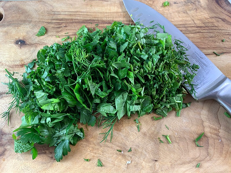 CHOPPED PARSLEY, DILL & MINT LEAVES ON A WOODEN CHOPPING BOARD WITH A SILVER KNIFE