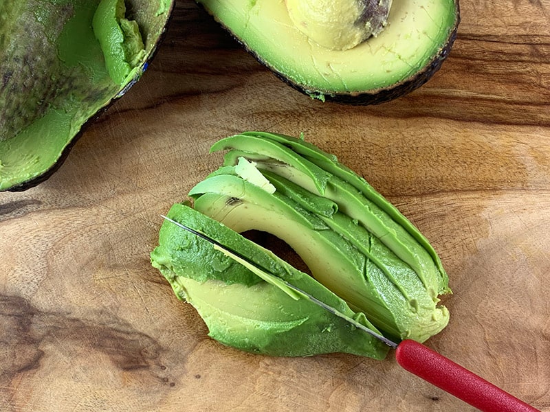 A close-up avocado being thinly sliced. 