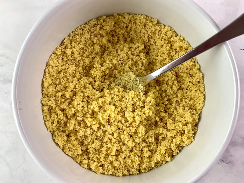 MIX OIL THROUGH COUSCOUS IN A WHITE BOWL WITH A FORK 