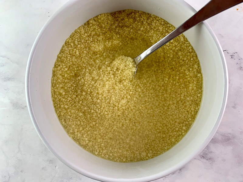 POURING BOILING WATER INTO COUSCOUS IN A WHITE BOWL