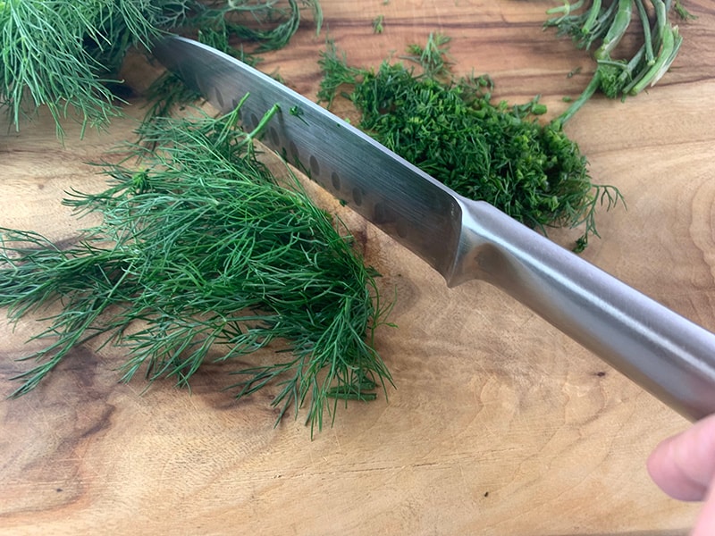 Chopping dill on a wooden board with a knife.