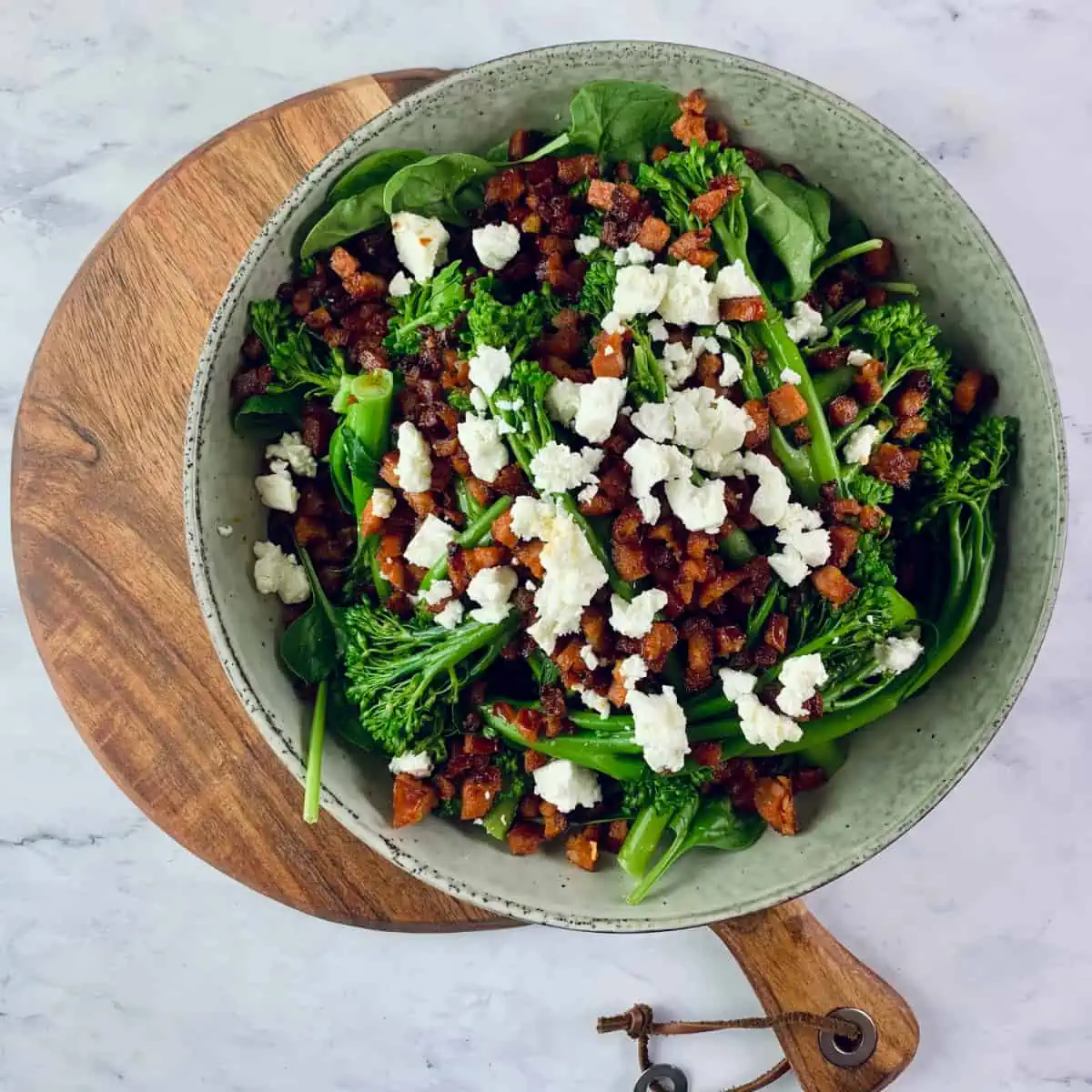 Broccolini salad with crispy chorizo and feta in a ceramic bowl with gold servers.